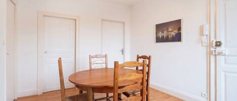 Un comedor con una mesa redonda de madera y cuatro sillas, paredes blancas y una lámpara en el techo.