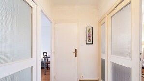 Ein Flur mit einer weißen Tür, einem gerahmten Bild an der Wand und einem Stuhl im Hintergrund.