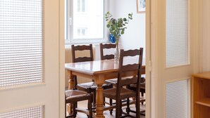 Ein Essbereich mit Holztisch und Stühlen, einer Pflanze im Blumenvasen und einem Fenster mit Jalousien.