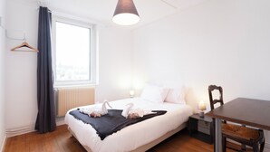 Ein ordentlich eingerichtetes Schlafzimmer mit Bett, Nachttisch, Sessel und einem Fenster mit Vorhängen.