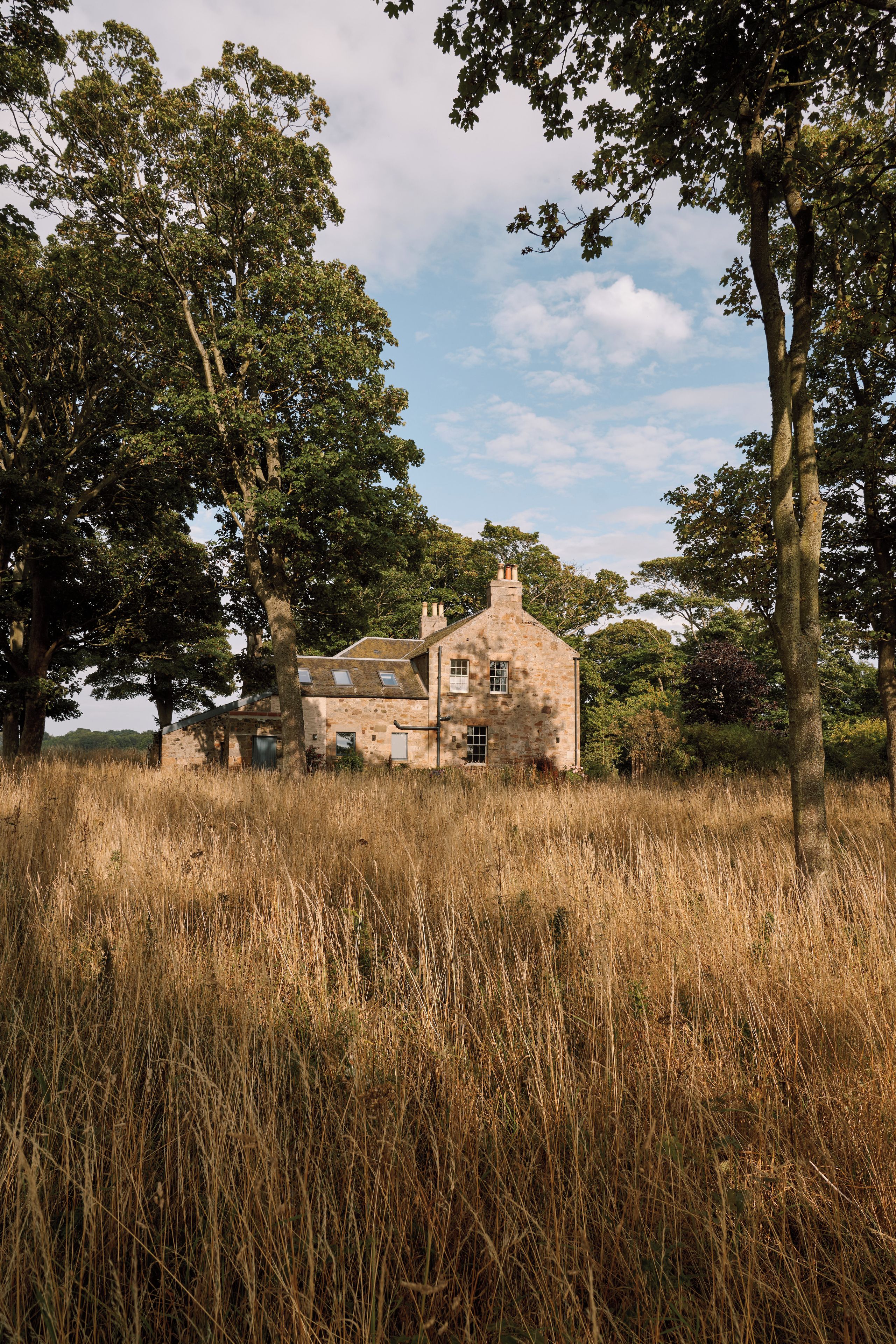 Een stenen huis, omringd door hoog gras en bomen.