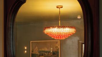 A mirror with a decorative frame reflecting a chandelier and a dining area.