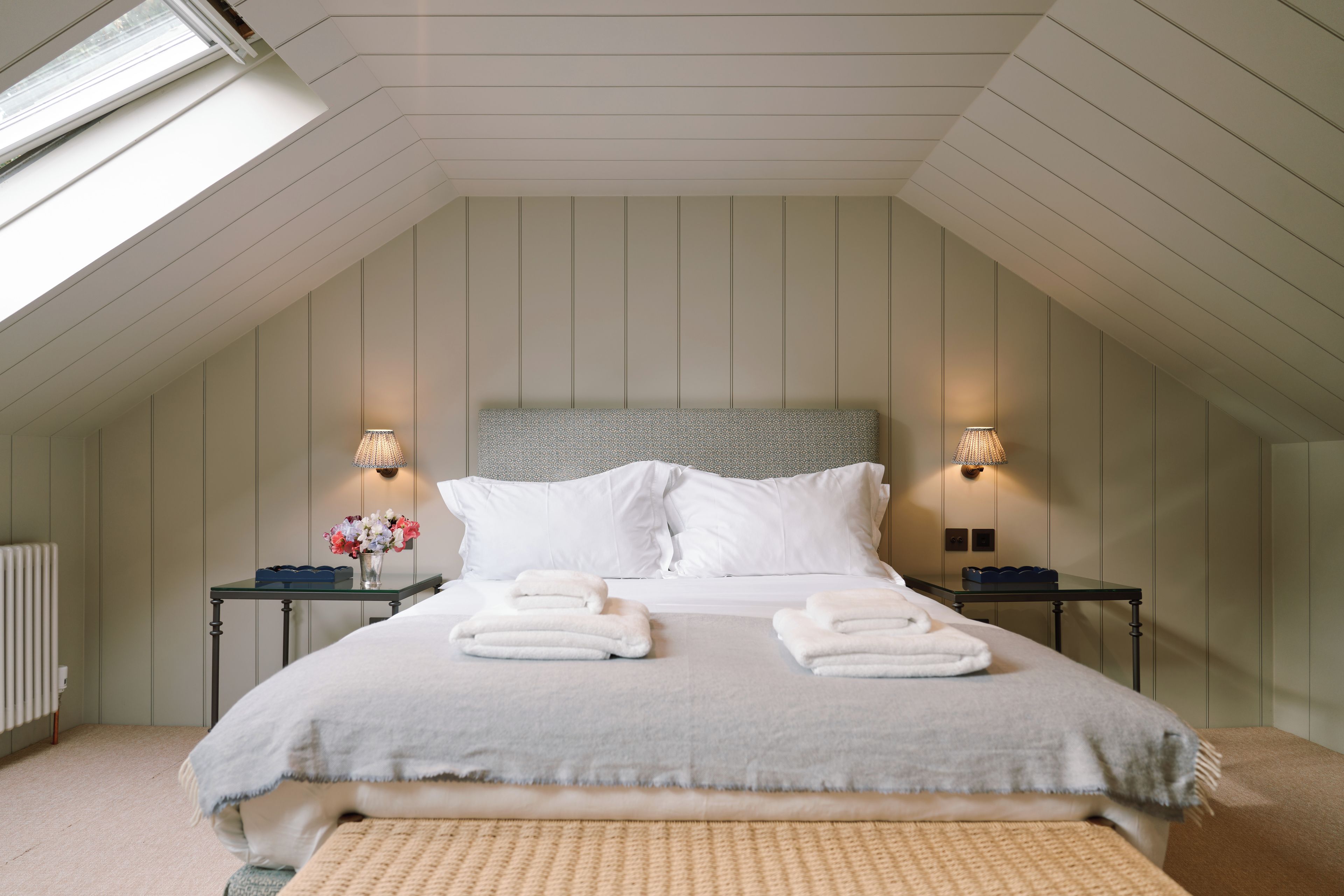 A bedroom with a sloped ceiling, a bed with white linens, two bedside lamps, and a radiator.