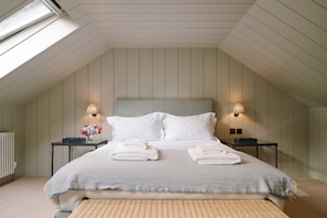 Una camera da letto con soffitto spiovente, un letto con lenzuola bianche, due lampade da comodino e un termosifone.