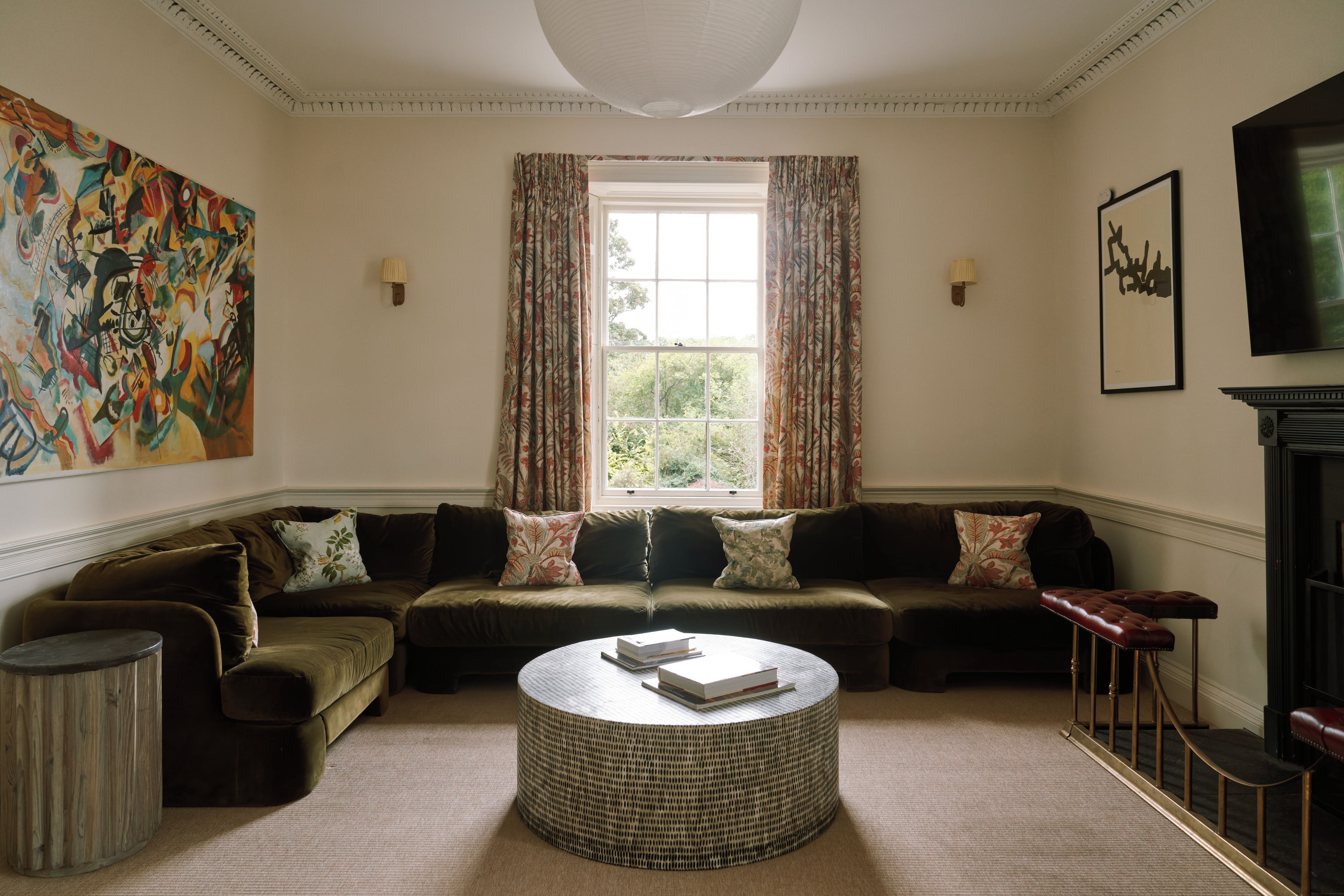 A living room with a sectional sofa, a round coffee table, and a large window with curtains.