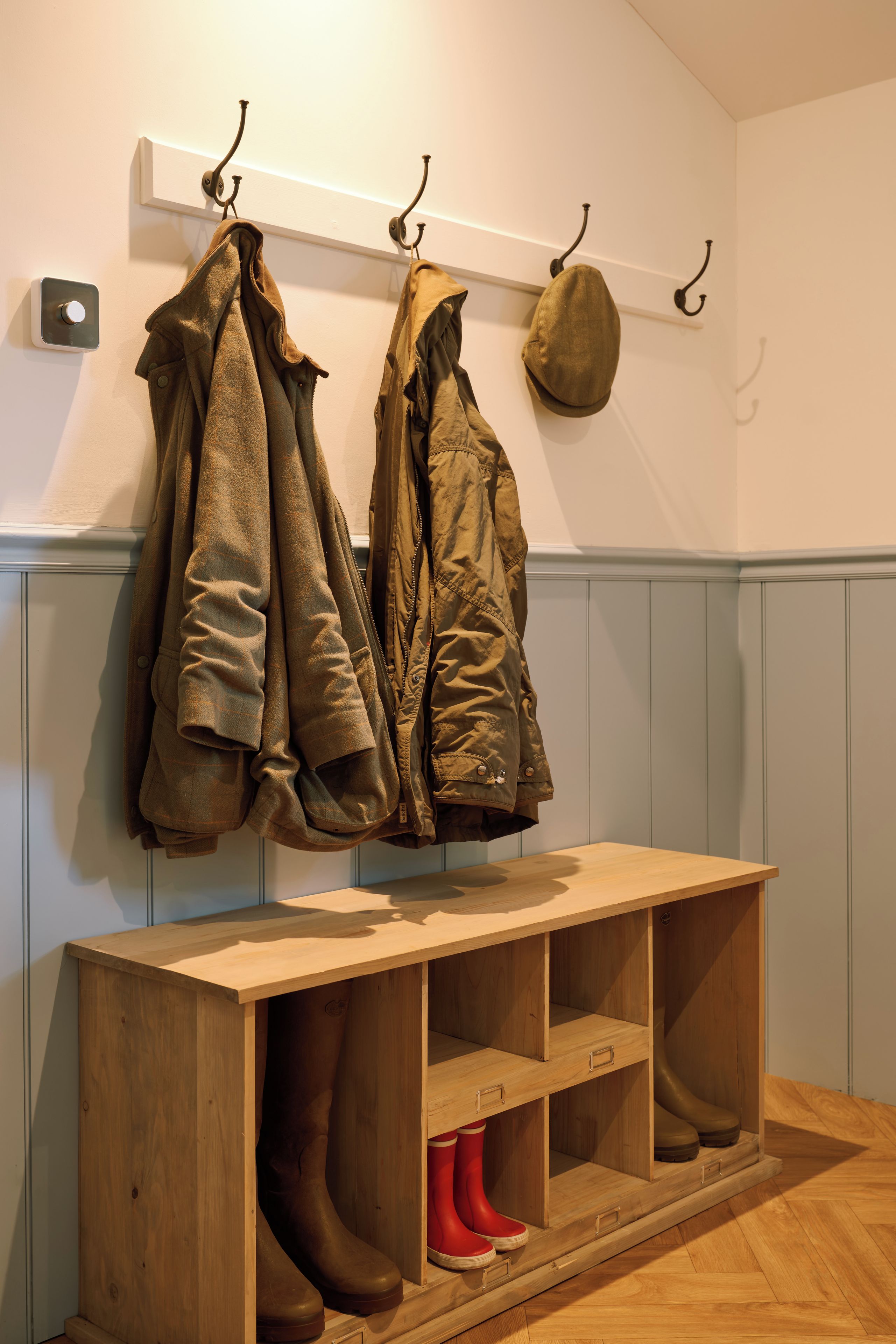A wooden bench with storage drawers, a coat rack with two coats and a hat, and a pair of boots.