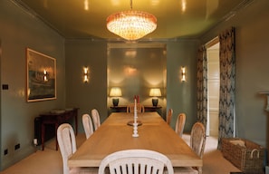 A dining room with a long wooden table, six chairs, two wall-mounted lamps, and a large chandelier. - West Muircambus Farmhouse (Kilconquhar)