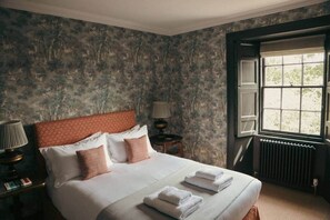 A bedroom with a bed, a nightstand, a lamp, a window, and a radiator. - West Muircambus Farmhouse (Kilconquhar)