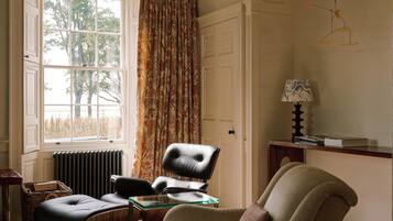 Een kamer met een groot raam, een radiator, een bureau met een lamp en twee stoelen.