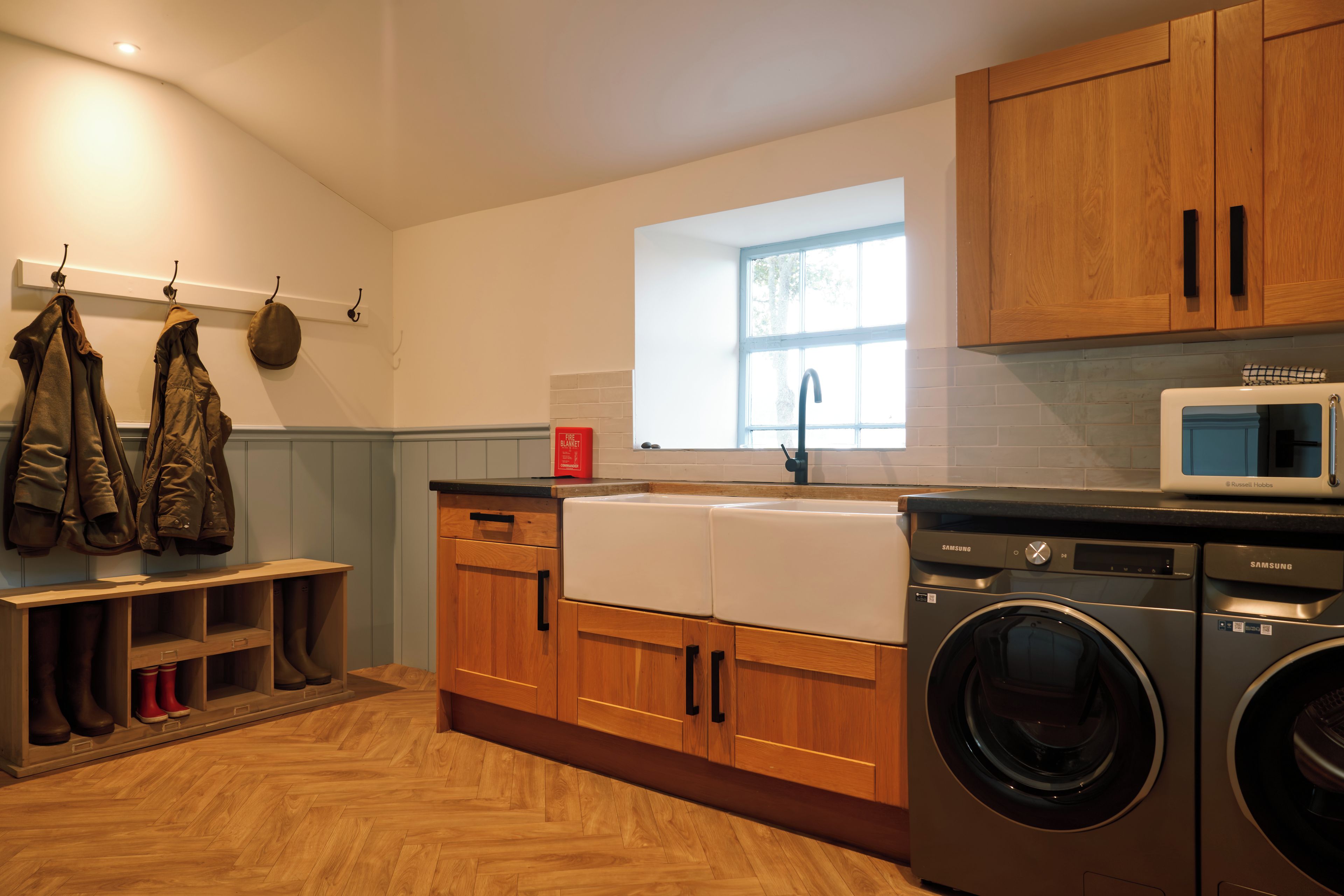 A modern kitchen with wooden cabinets, a built-in washing machine, and a window providing natural light.