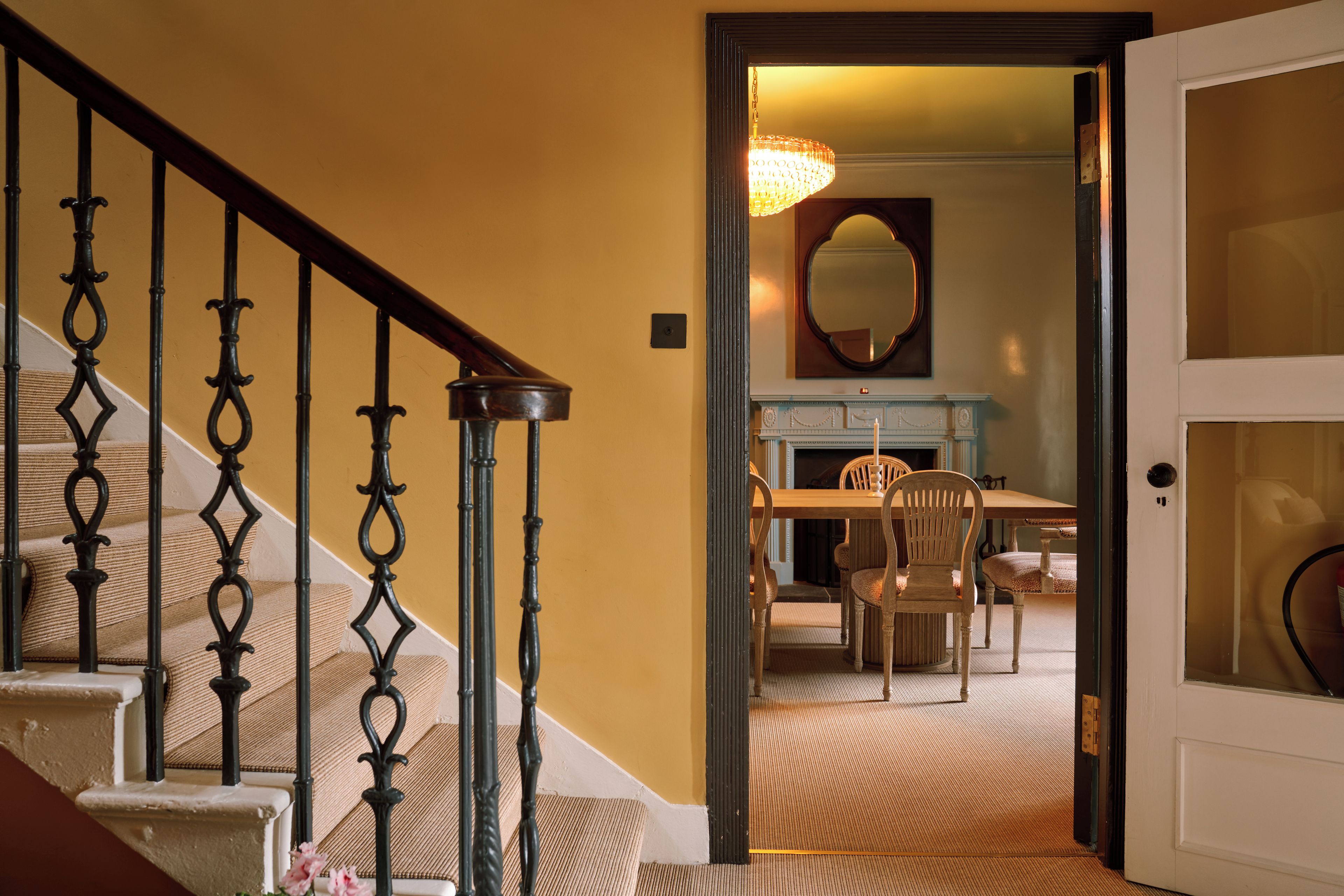 A staircase with ornate black balusters leading to a room with a dining table and chairs.
