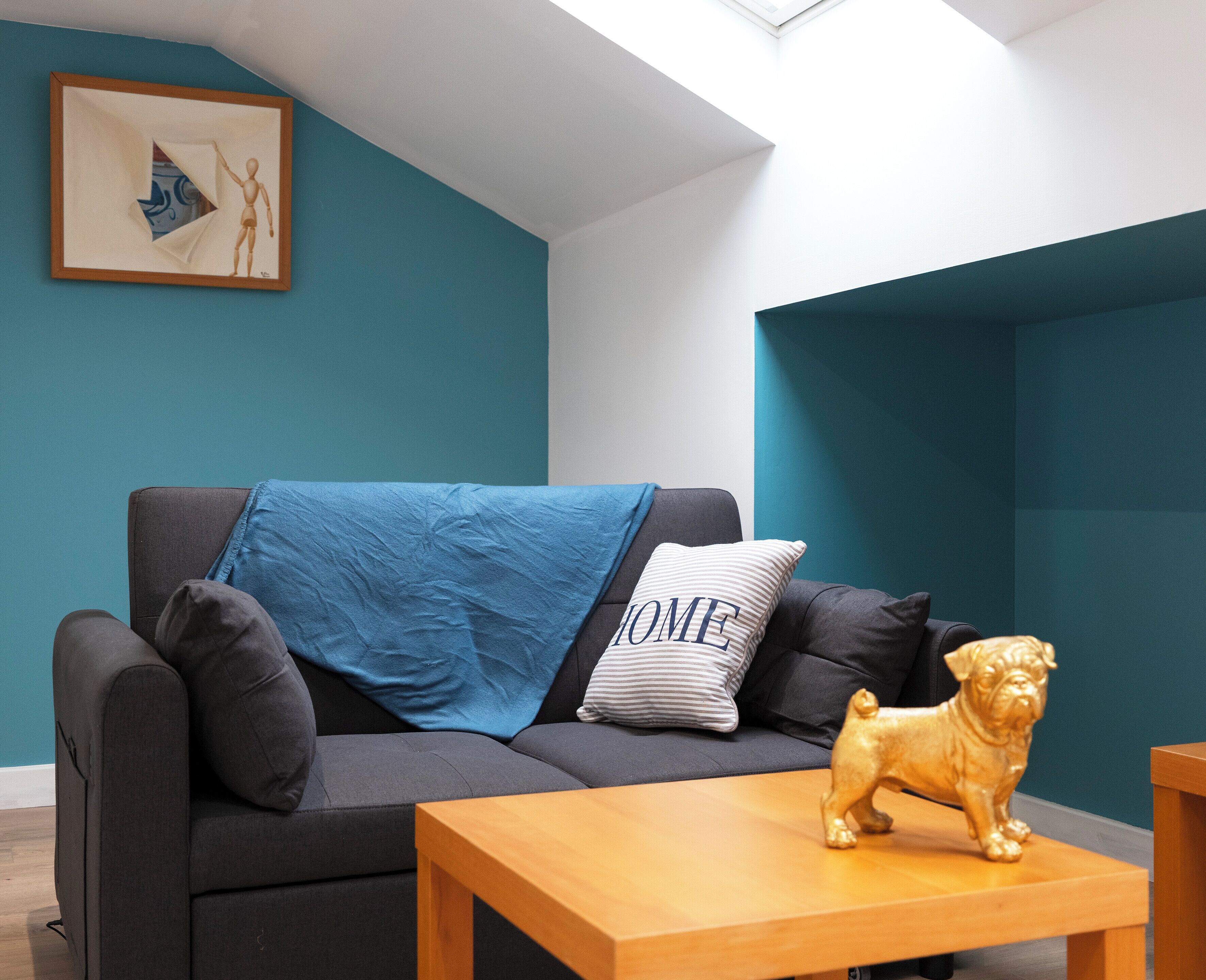 A modern living room with teal walls, a dark grey sofa, a wooden coffee table, and a golden dog statue.