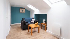 A modern living room with a skylight, a sofa, a coffee table, and a small table with a decorative item. - Hôtel des Cousines – Emma Apartment (Nancy)