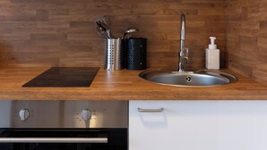 A modern kitchen with wooden backsplash, stainless steel sink, and built-in appliances. - Hôtel des Cousines   – Emma Apartment (Nancy)