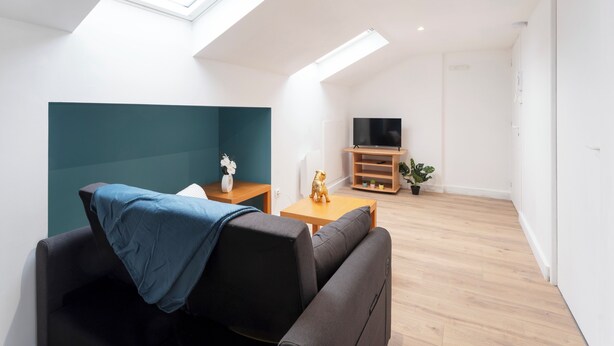 A modern living room with a sofa, a small table, a TV, and a skylight. - Hôtel des Cousines – Emma Apartment (Nancy)