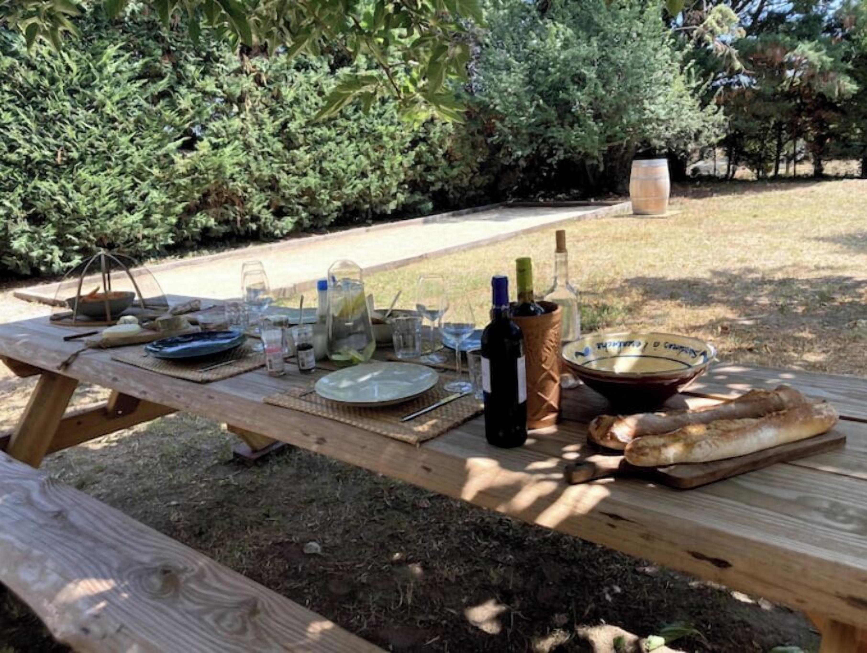 A picnic table set outdoors with various food items, glasses, and bottles.