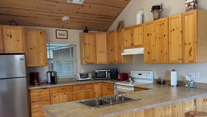 Una cocina moderna con armarios de madera, un refrigerador de acero inoxidable, un microondas y un lavamanos. Hay tres taburetes de madera en la isla.