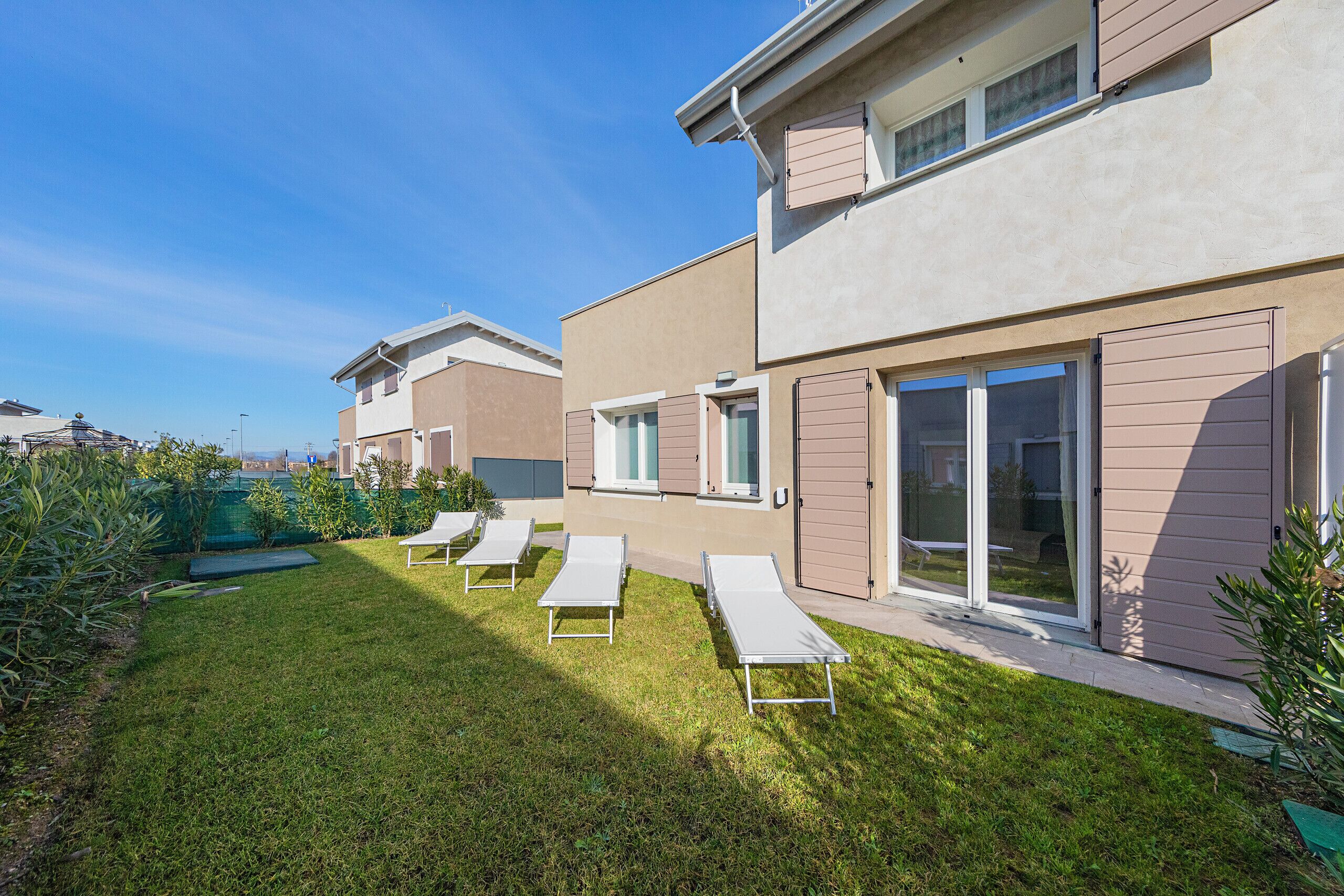 A modern residential building with a well-maintained lawn, outdoor seating area, and large sliding glass doors.