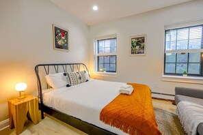A bedroom with a bed, bedside lamp, two windows, and a small table. - Quiet Studio Circa South End (Boston)