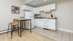 Une cuisine moderne avec des meubles blancs, une table en bois, deux tabourets et une petite plante en pot.