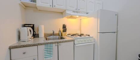 Cocina compacta con gabinetes blancos, estufa a gas, pileta y refrigerador.