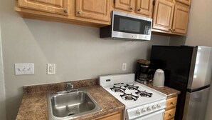 A kitchen with wooden cabinets, a stainless steel sink, a stove, a microwave, a refrigerator, and a coffee maker. - Comfy Back Bay Alcove Studio Apt (Boston)