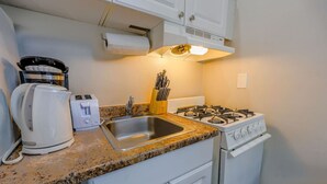 A compact kitchen with a gas stove, a coffee maker, a toaster, and a sink.
