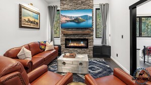 A living room with a stone fireplace, leather sofas, a mounted TV, and a framed painting.