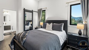 A modern bedroom with a large bed, a nightstand, a dresser, and a window with curtains.