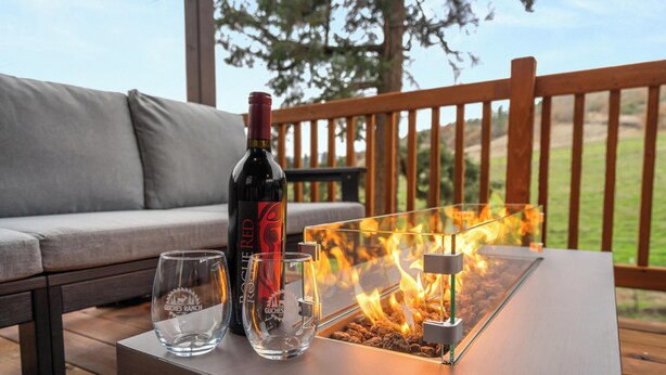 A bottle of red wine, two glasses, and a glass fire feature on a table.