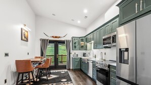 A modern kitchen with green cabinets, stainless steel appliances, and a dining area with leather chairs.