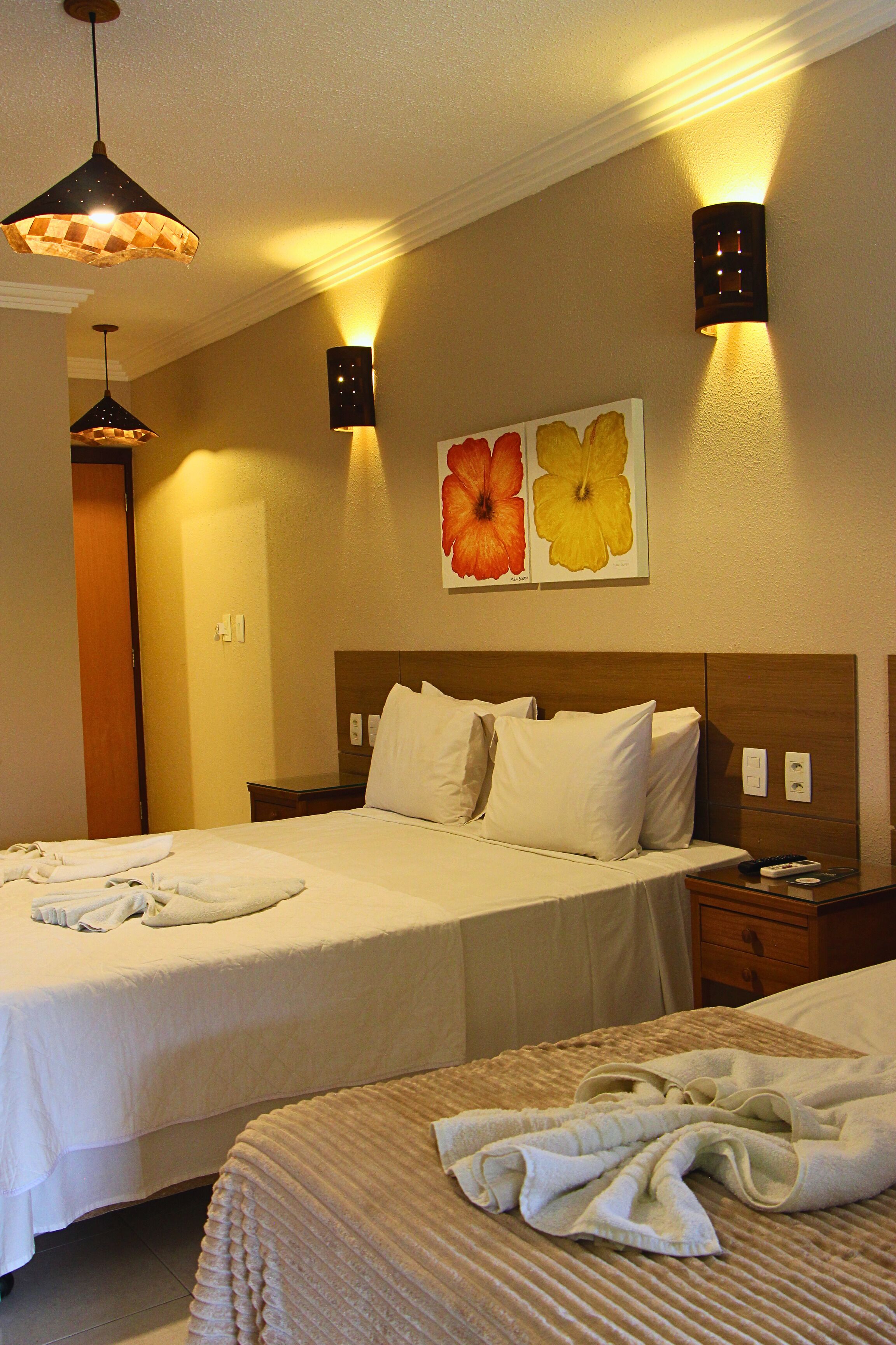 A hotel room with two beds, a nightstand, a lamp, and a wall-mounted light fixture.