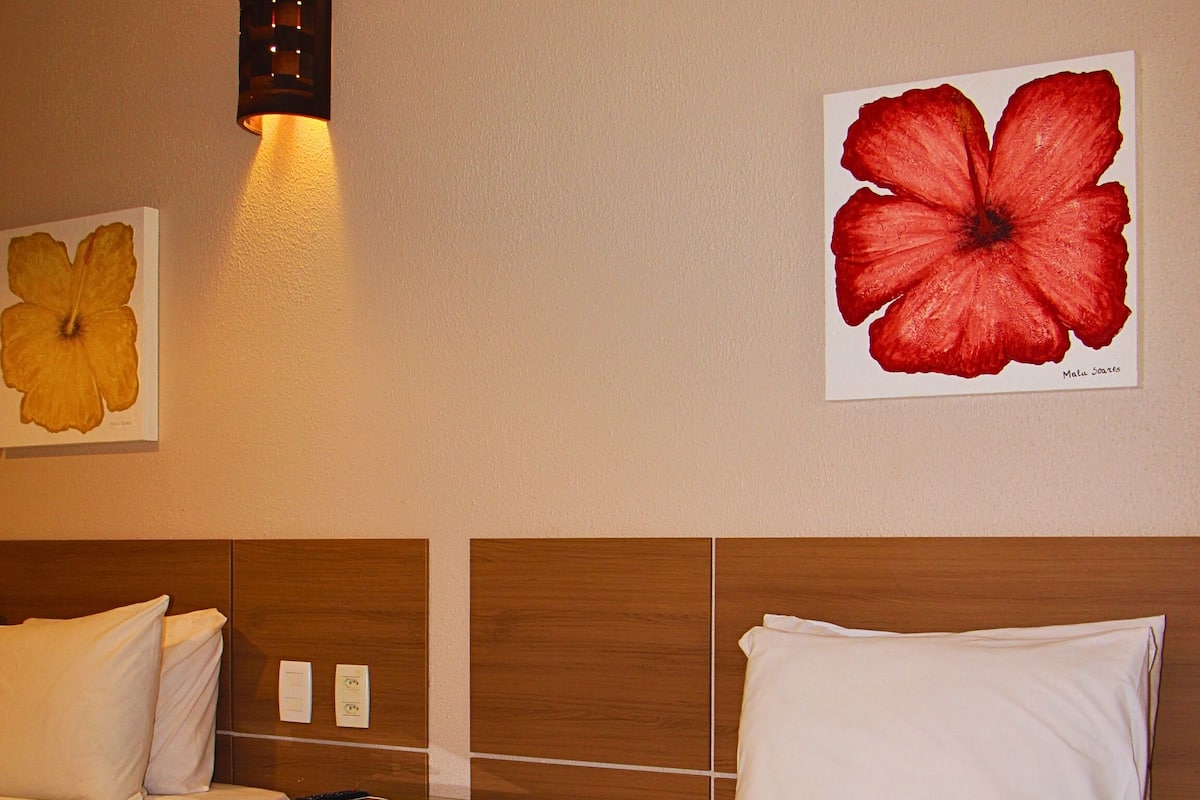 Habitació d'hotel amb dos llits, una taula de nit, una làmpada penjada a la paret i dues obres d'art mural.