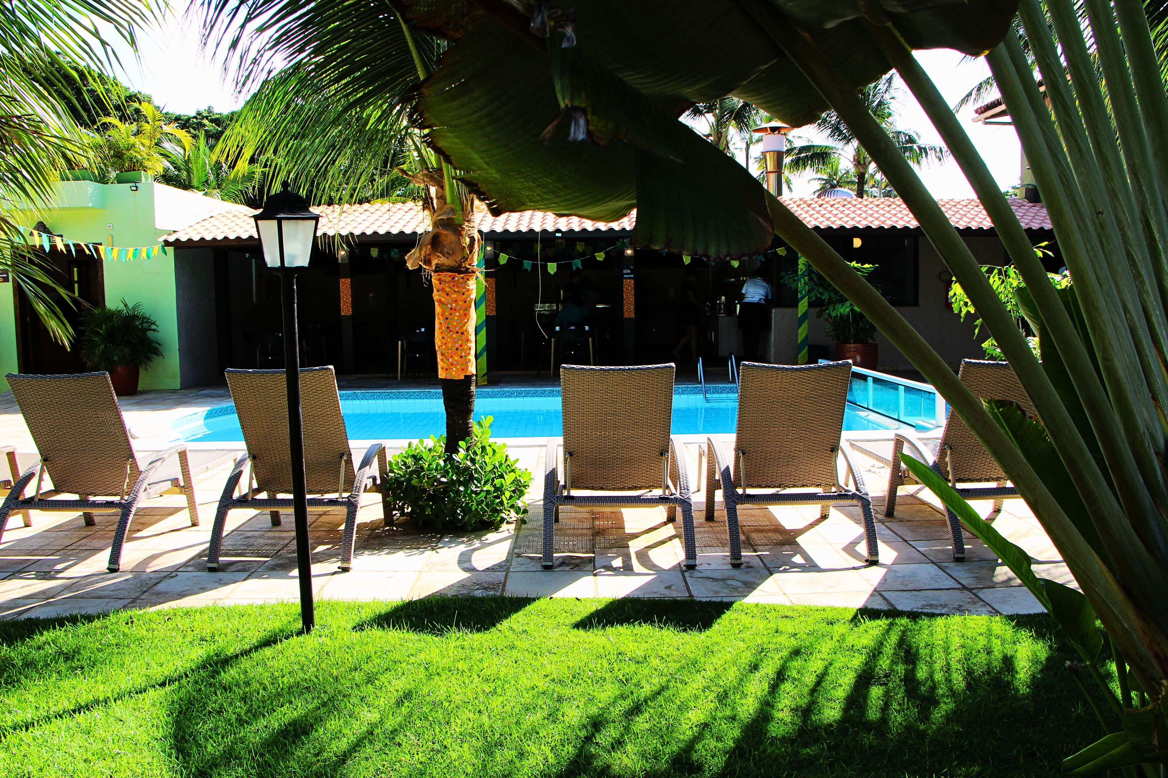 A poolside area with lounge chairs, a pool, and a building with a tiled roof.