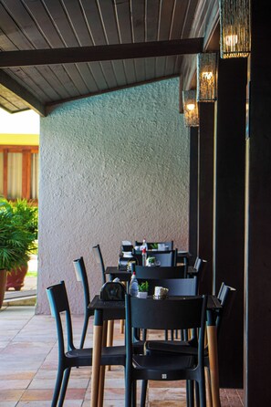 An outdoor patio area with tables and chairs, a textured wall, and hanging lights. - POUSADA PORTO MAR (Ipojuca)