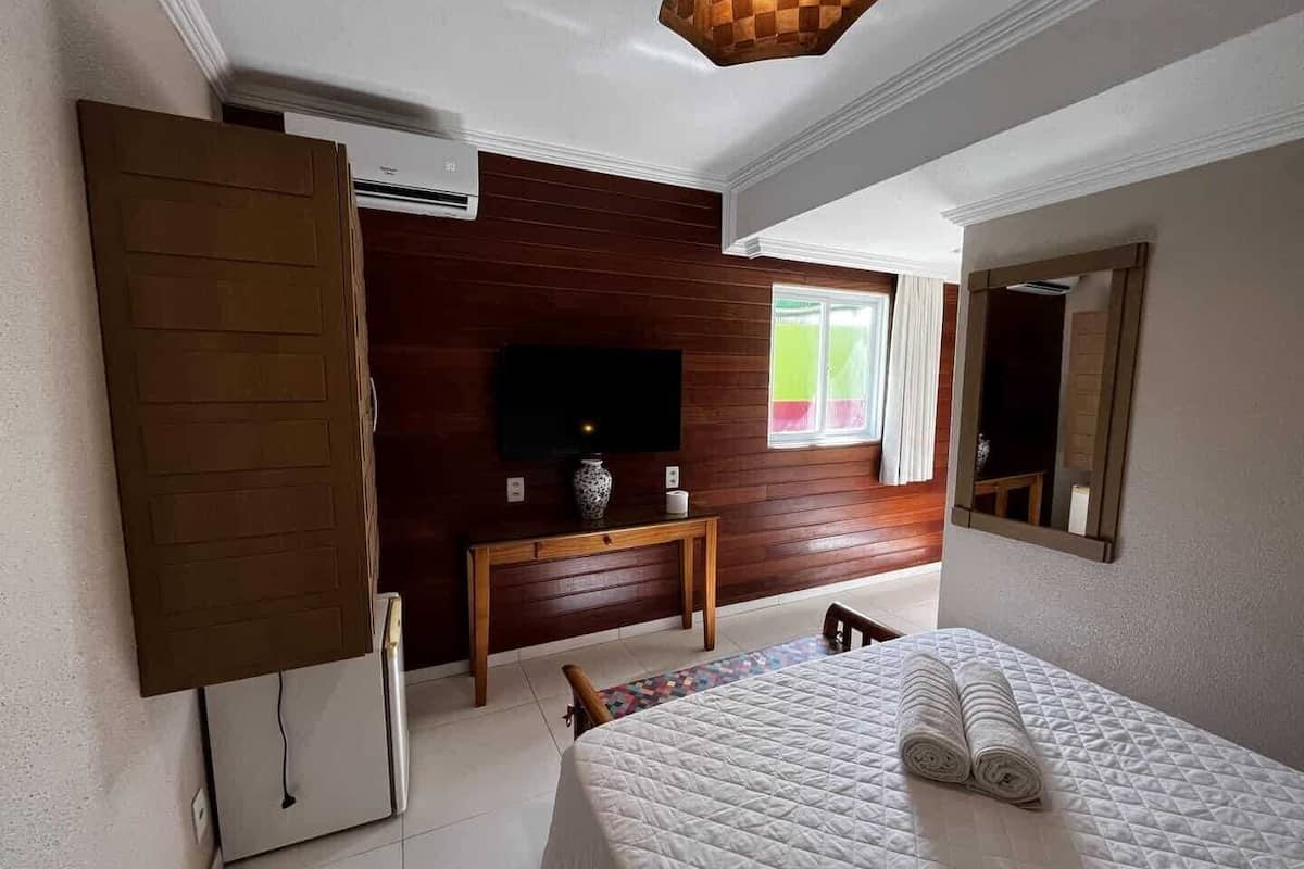 Una habitació d'hotel amb un llit, una televisió penjada a una paret de fusta, un escriptori i un mirall.