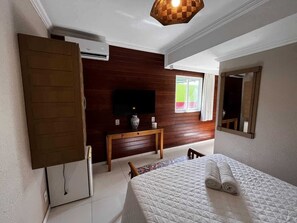 Ein Hotelzimmer mit Bett, Fernseher an einer Holzwand, Schreibtisch und Spiegel.