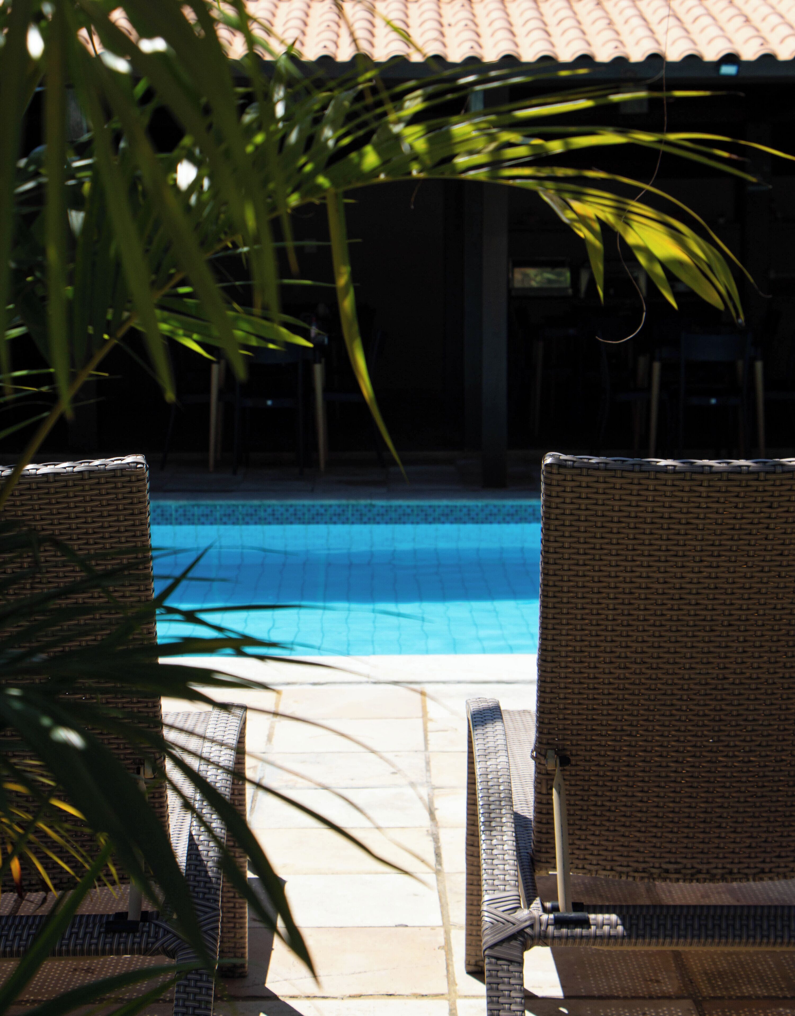 Un área de piscina con sillones de mimbre y suelo de baldosas.