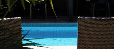 Un área de piscina con sillones de mimbre y suelo de baldosas.