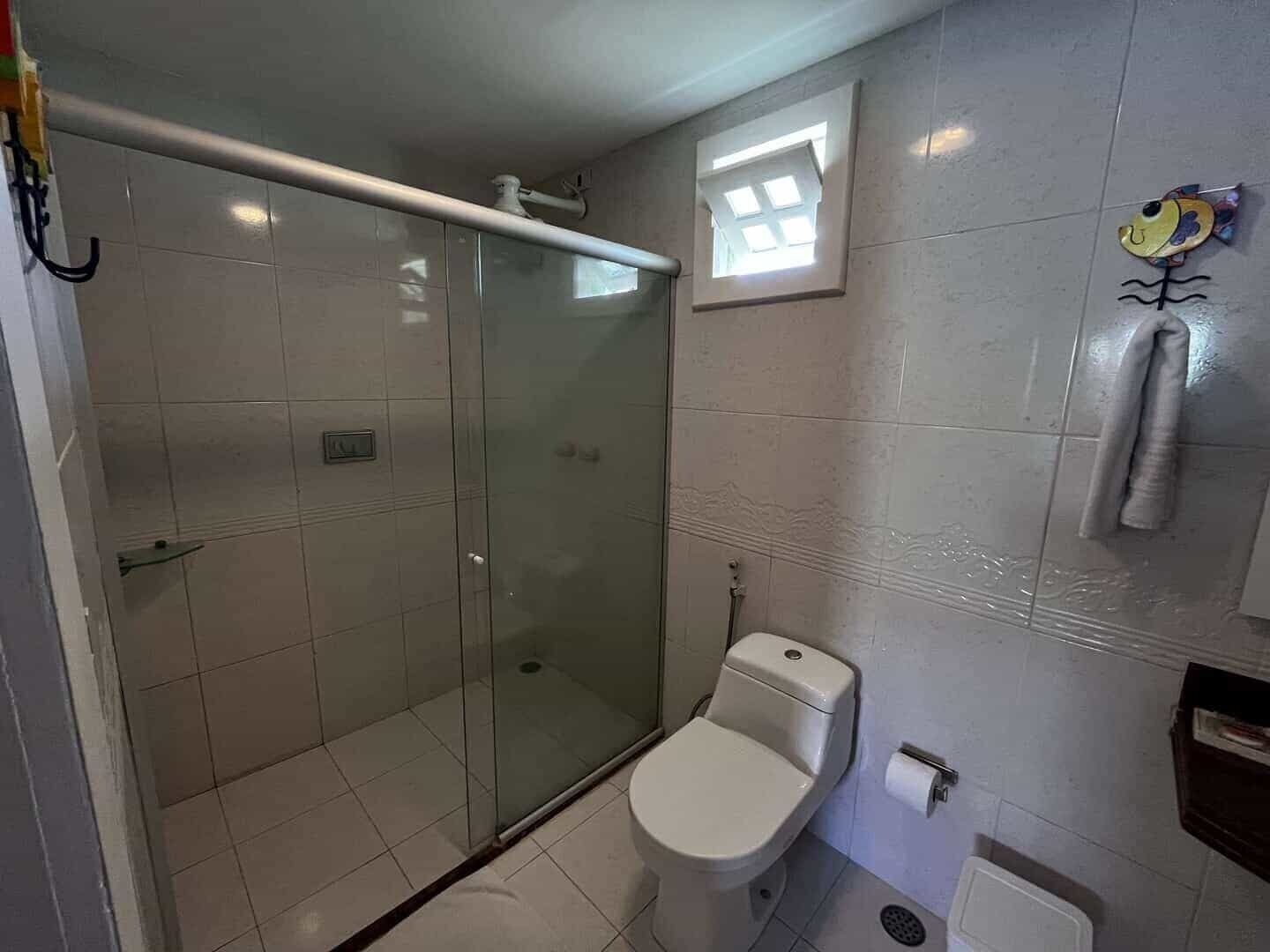A bathroom with a glass-enclosed shower, a toilet, and a small window.