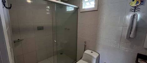 A bathroom with a glass-enclosed shower, a toilet, and a small window.
