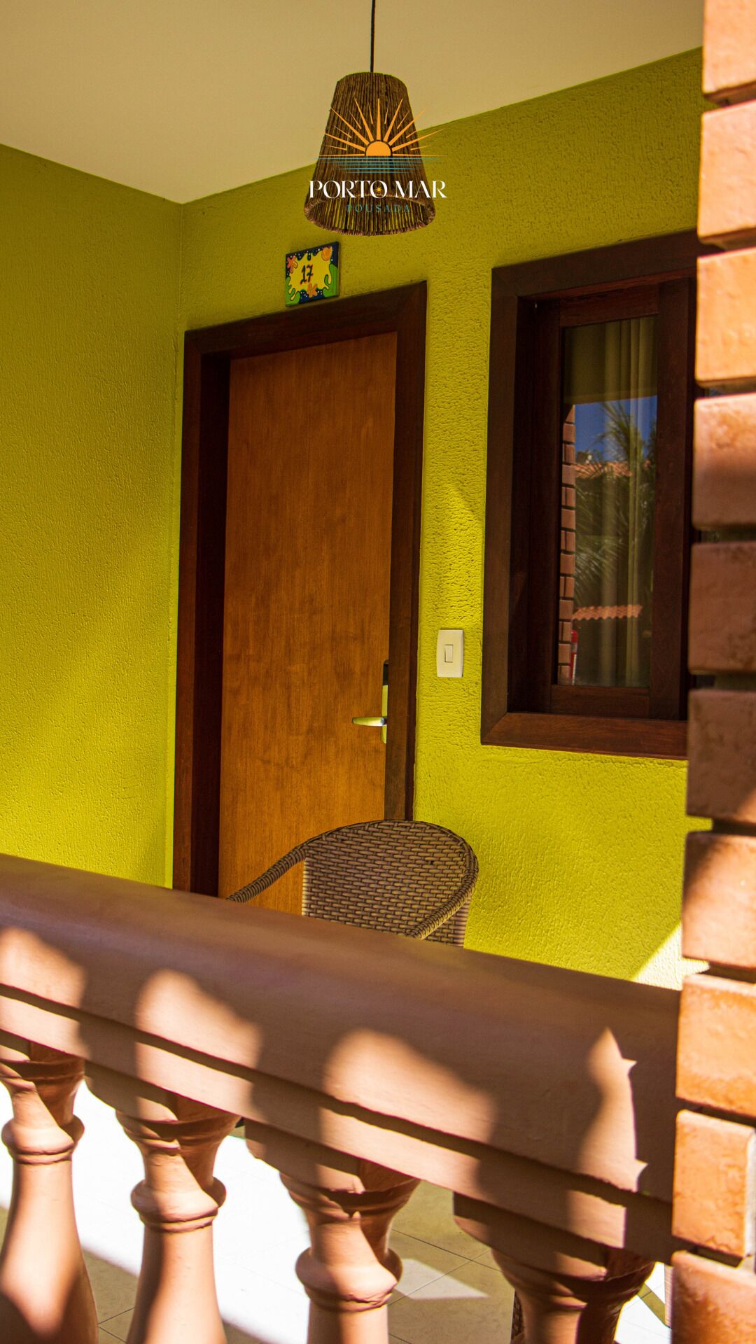 A room with a wooden door, a wicker chair, a window with curtains, and a hanging light fixture.