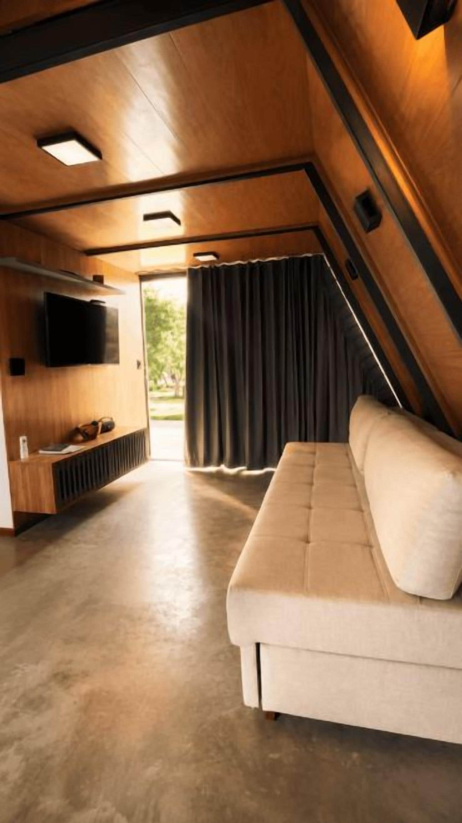 Um interior acolhedor com um sofá, uma televisão de tela plana e uma janela com cortinas.