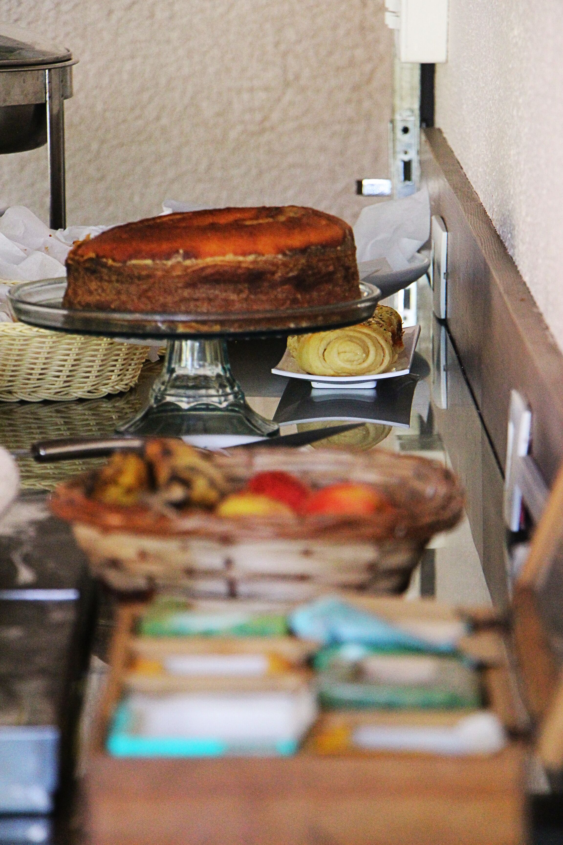 A buffet setup with a cake on a stand, a basket of pastries, and a tray of sliced fruit.