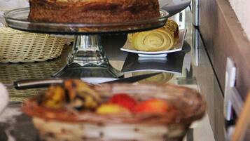 A buffet setup with a cake on a stand, a basket of pastries, and a tray of sliced fruit.
