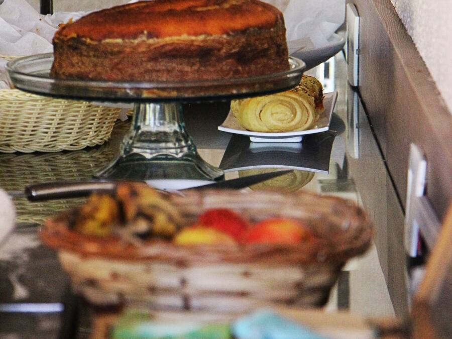 A buffet setup with a cake on a stand, a basket of pastries, and a tray of sliced fruit.