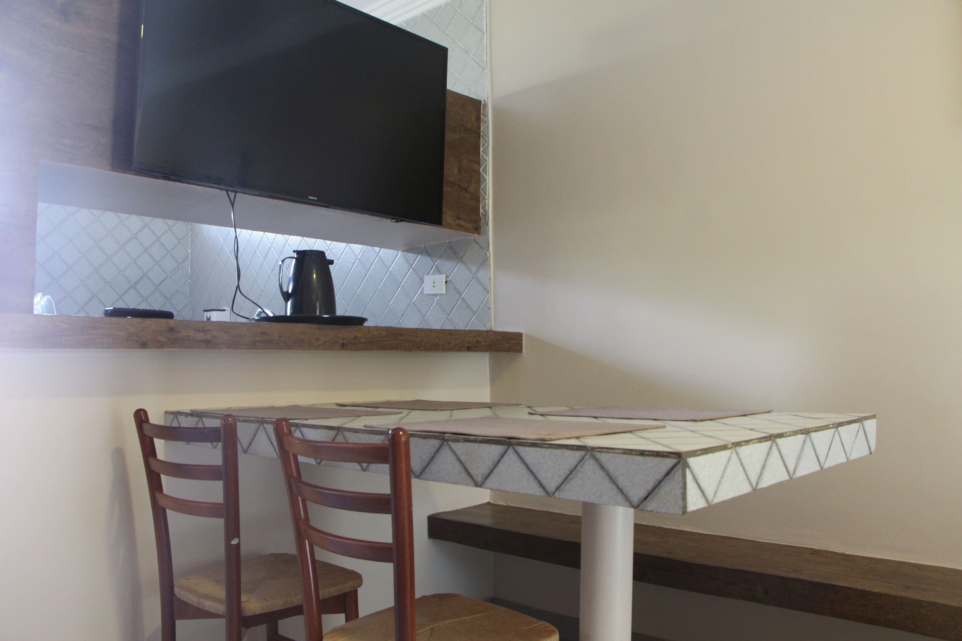 A kitchen with a flat-screen TV mounted above a countertop, a coffee maker, and two wooden chairs.