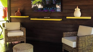 A room with wicker furniture, a television mounted on the wall, and a ceiling with a wooden design. - POUSADA PORTO MAR (Ipojuca)