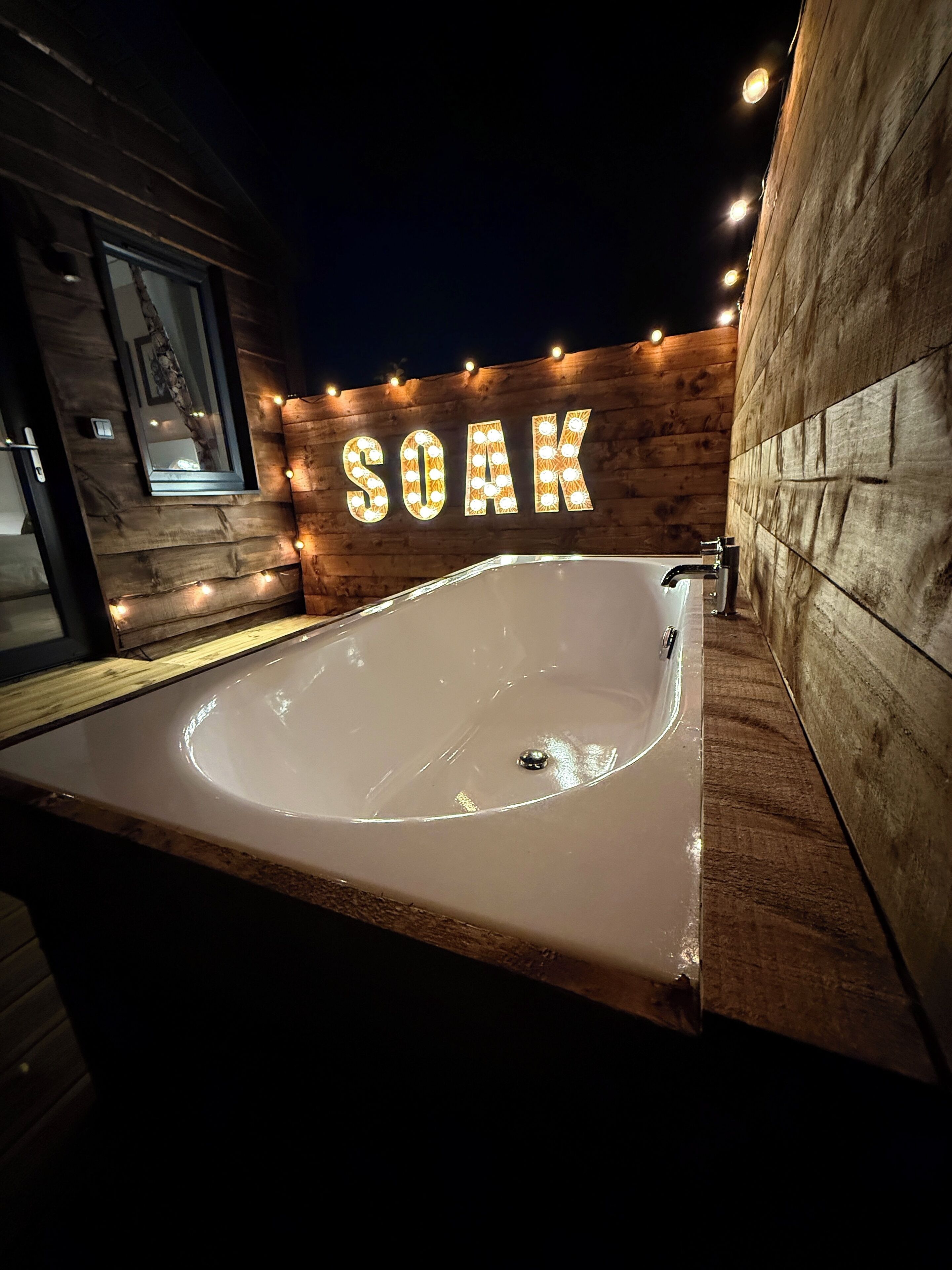 A wooden cabin with a large bathtub labeled "SOAK" and string lights.