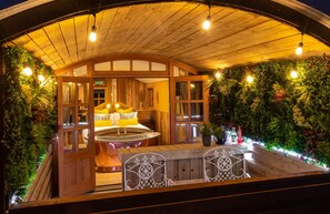 A cozy outdoor seating area with a wooden bench and a table, surrounded by lush greenery and a wooden pergola.